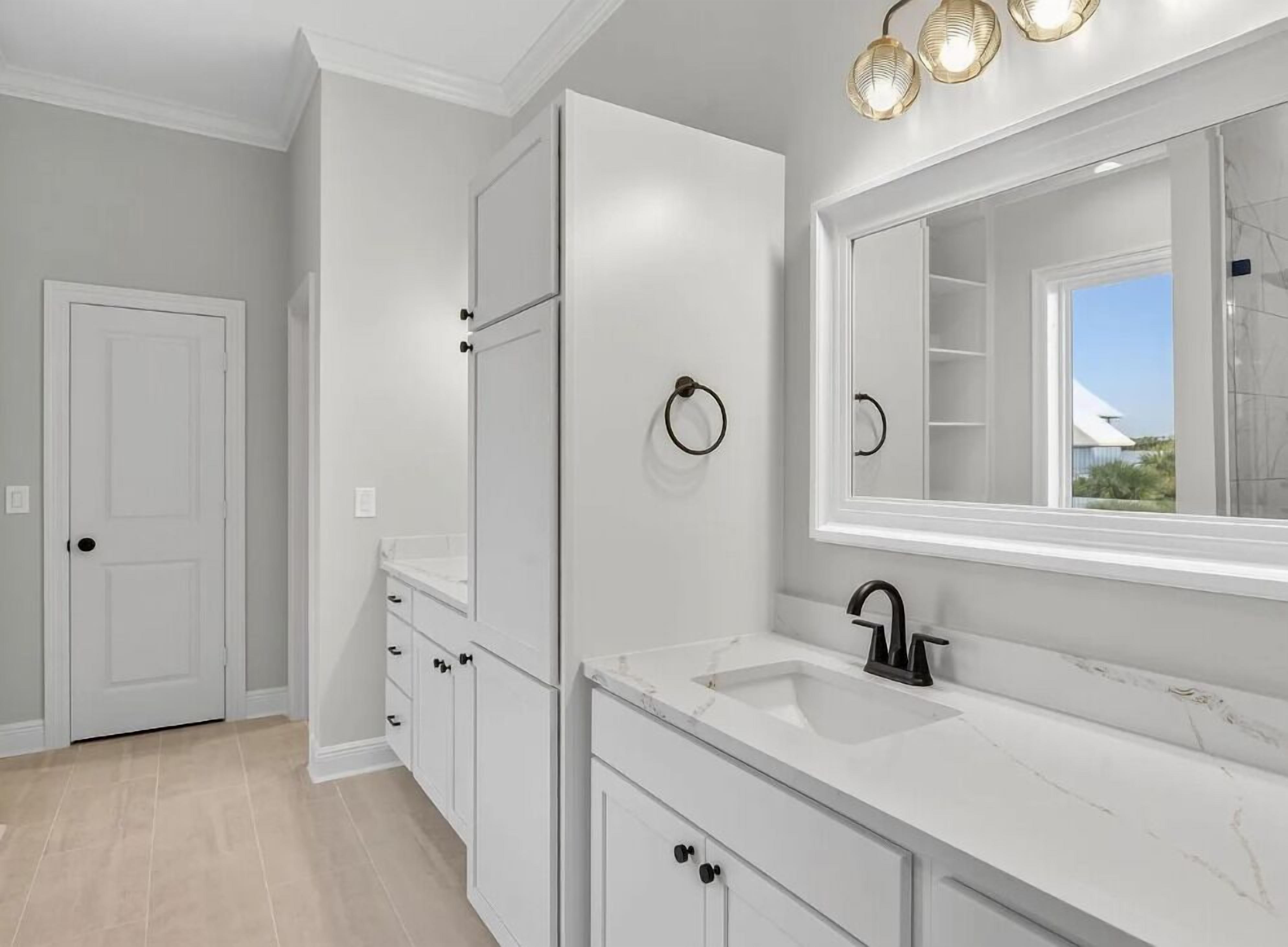 Une salle de bain dotée d’un grand miroir, de meubles blancs, d’un robinet noir et d’un porte-serviettes.