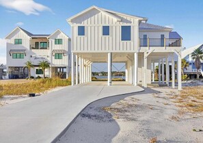 A coastal house with a covered porch, multiple windows, and a clear sky. - Salt Water Heals Everything (Gulf Shores)