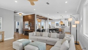 A spacious living room with a large sectional sofa, a wooden accent wall, and a dining area visible through an open door. - Salt Water Heals Everything (Gulf Shores)
