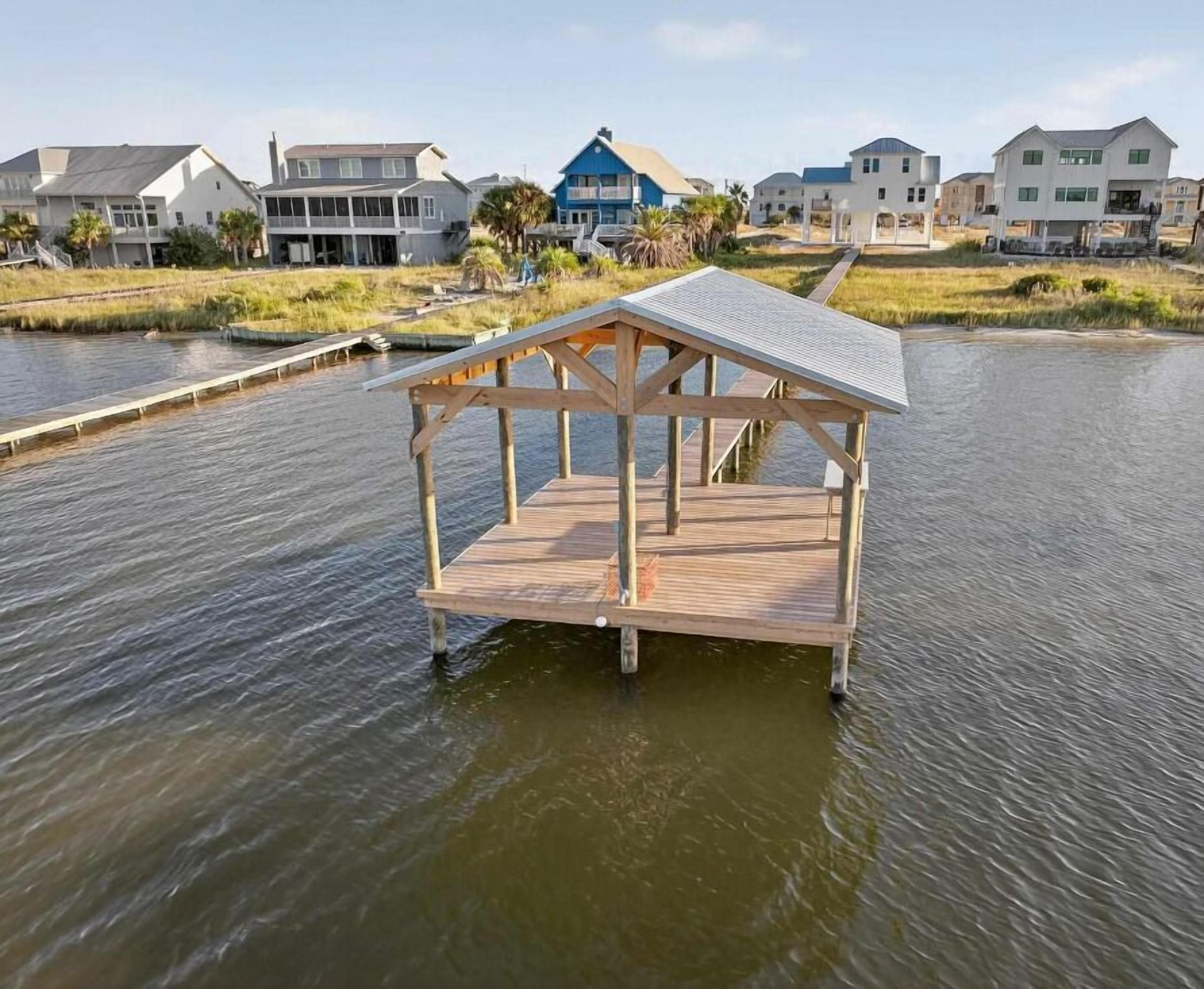 A wooden dock with a covered area, surrounded by water and houses in the background.