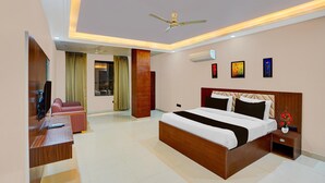 Ein Hotelzimmer mit Bett, Schreibtisch, Fernseher, Deckenventilator und Bildern an der Wand.