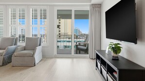 Een moderne woonkamer met een grote televisie, een bank, een eettafel en een balkon met uitzicht op een zwembad.