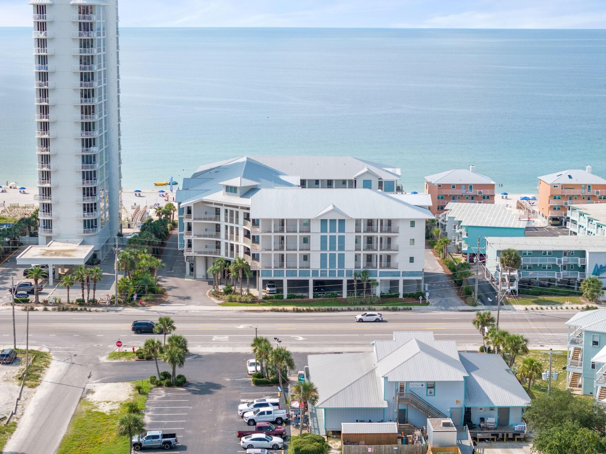 A coastal hotel with multiple floors, a parking lot, and a view of the beach and ocean.