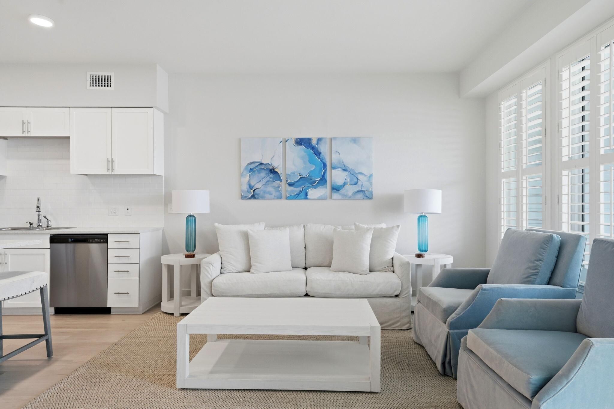Un salon moderne avec un canapé blanc, un fauteuil bleu, une table basse blanche et un tableau abstrait bleu accroché au mur.