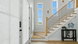 A staircase with wooden steps and black railings, a white door with a window, a blue floral rug, and a small table with decorative items. - 66 Parks Edge (Orange Beach)