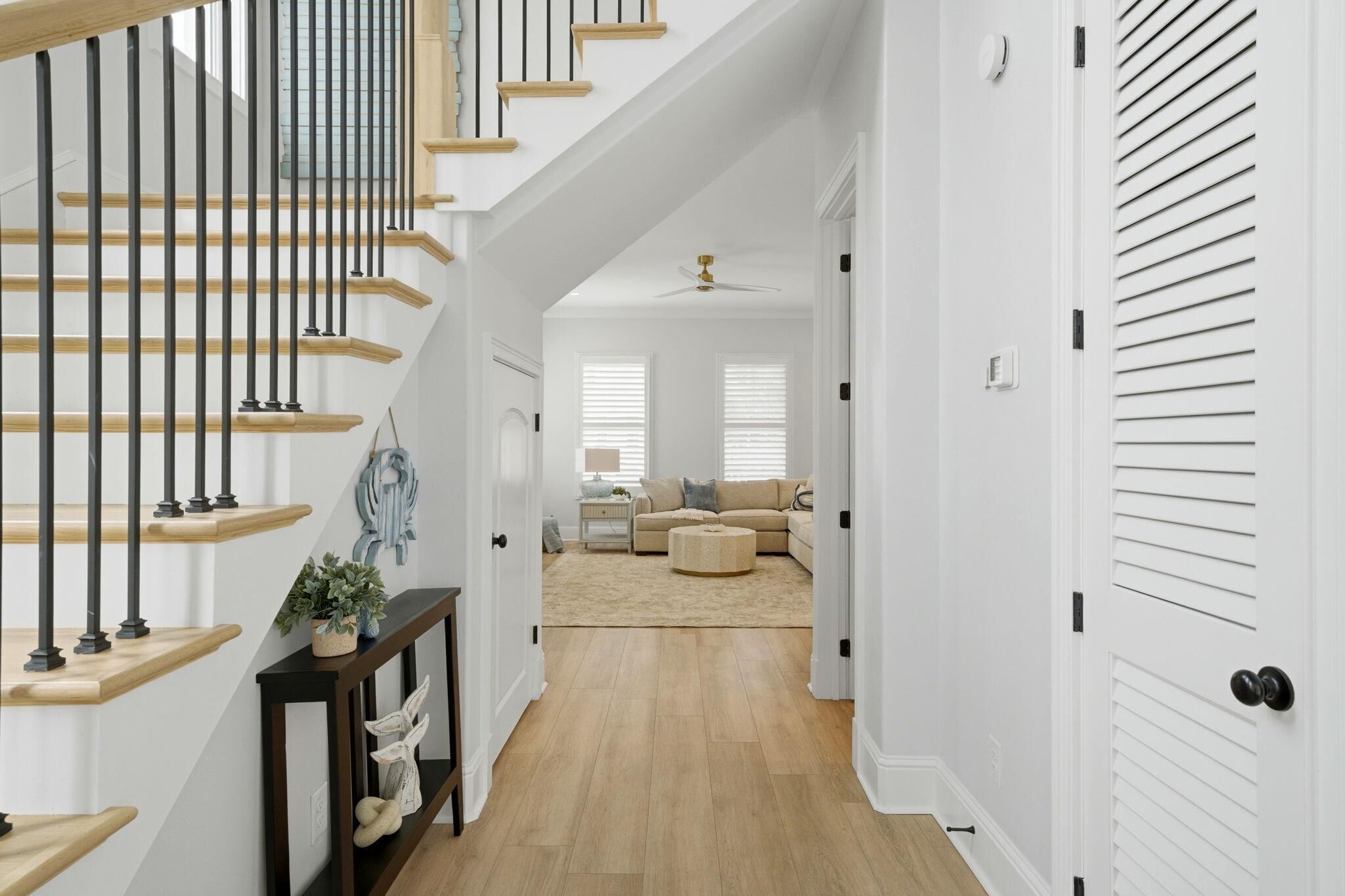 Una escalera con escalones de madera y barandales negros, un pasillo con alfombra color beige y una puerta blanca con paneles verticales.