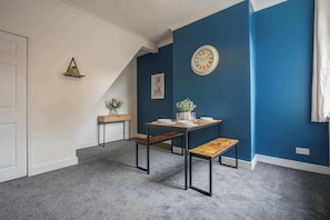 Una habitación con una pared azul de acento, un reloj de pared redondo, una pequeña mesa con un banco y una puerta.