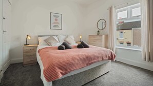 A bedroom with a bed, bedside tables, a window with curtains, a wall-mounted mirror, and a framed picture. - Central Grimsby House w/ Free Parking & Garden (Grimsby)