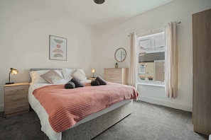 Un dormitorio con cama, mesitas de noche, un espejo y una ventana con cortinas.
