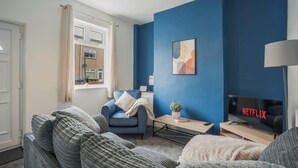 A living room with a blue accent wall, a sofa, a chair, a TV displaying 'NETFLIX,' and a lamp. - Central Grimsby House w/ Free Parking & Garden (Grimsby)