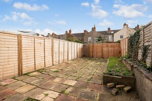 A paved backyard with a wooden fence, a brick wall, and a small garden area.