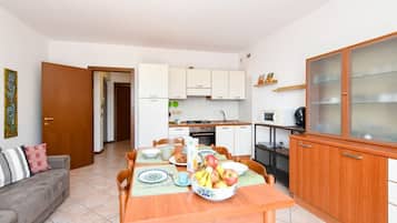 A compact living space with a dining table set for breakfast, a kitchenette, a sofa, and a cabinet with glass doors.