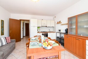 A compact living space with a dining table set for breakfast, a kitchenette, a sofa, and a cabinet with glass doors. - Casa Vuvi - Two-room apartment very close to the beach. (Toscolano Maderno)