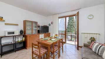 Un espace de vie compact comprenant un coin repas, une kitchenette et un balcon avec vue sur les arbres.