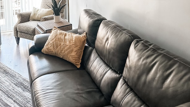 Ett modernt vardagsrum med en soffa i läder, en mönstrad fåtölj, en dekorativ väggdekoration och en golvlampa.