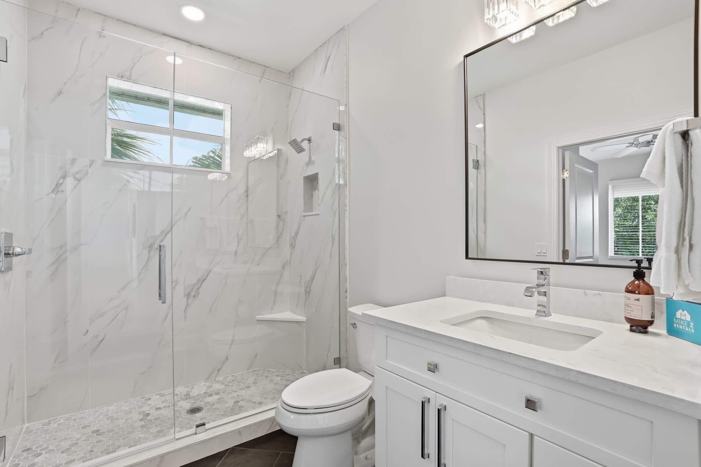 A modern bathroom with a glass-enclosed shower, a large mirror, and a white vanity with a sink.