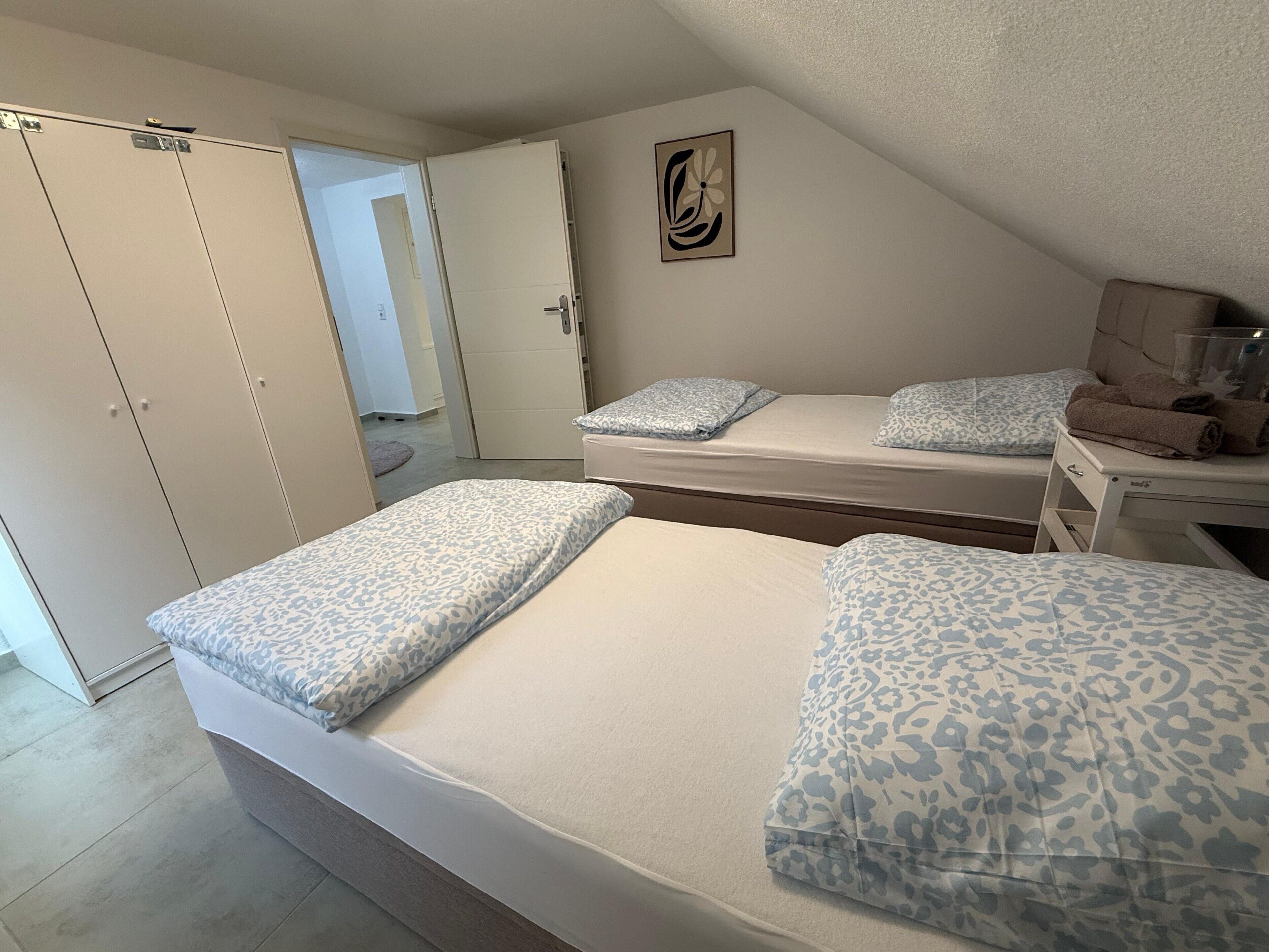 A bedroom with two beds, a wardrobe, and a small table with towels.
