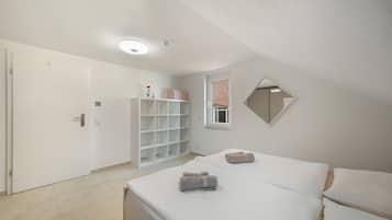Un dormitorio con cama, armario, espejo y ventana con vista a un muro de ladrillo.