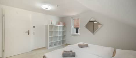 Une chambre à coucher comprenant un lit, une armoire, un miroir et une fenêtre donnant sur un mur en briques.