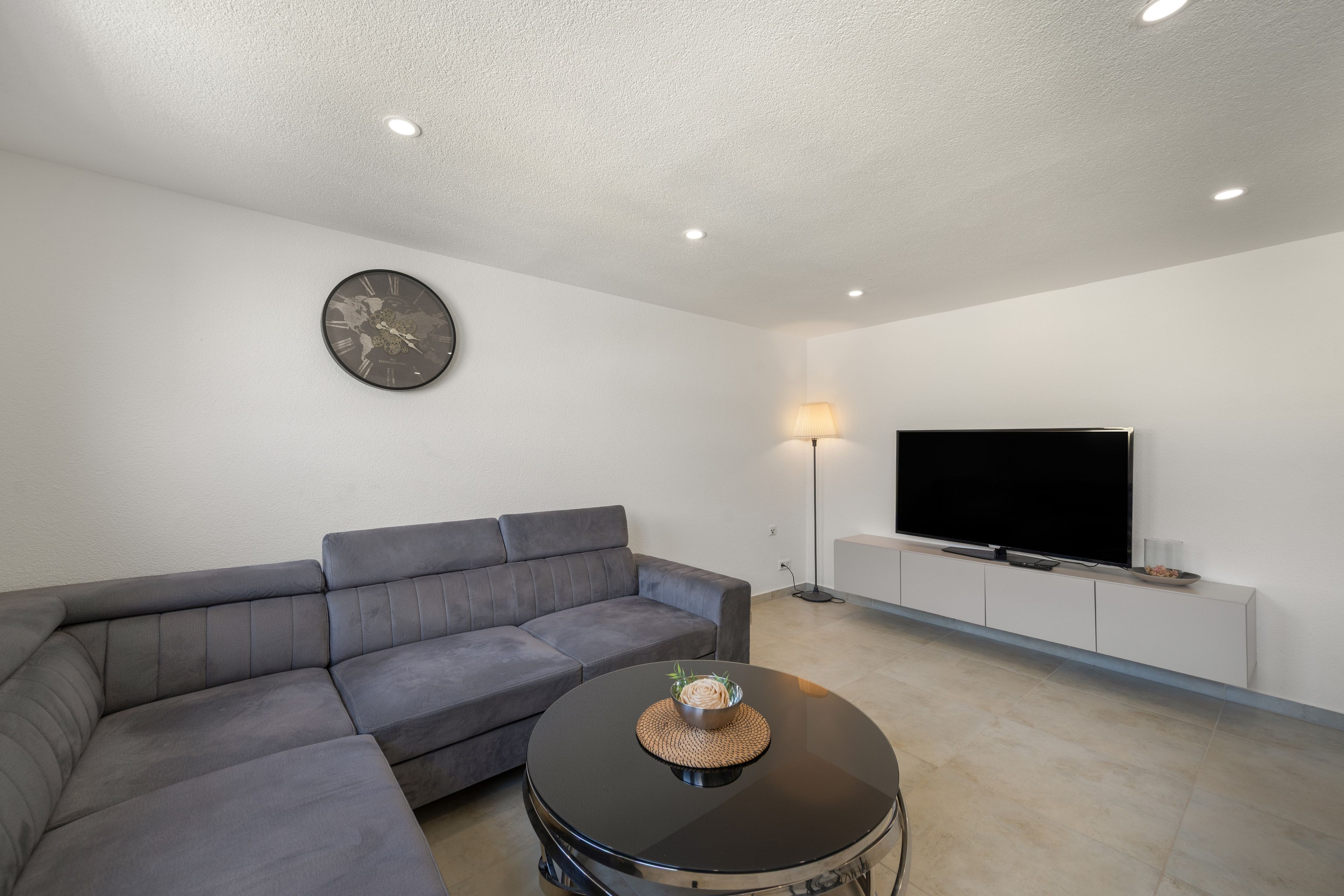 Una sala de estar moderna con un sofá modular, una mesa redonda de centro, un televisor de pantalla plana e iluminación empotrada en el techo.