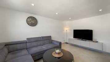 Una sala de estar moderna con un sofá modular, una mesa redonda de centro, un televisor de pantalla plana e iluminación empotrada en el techo.