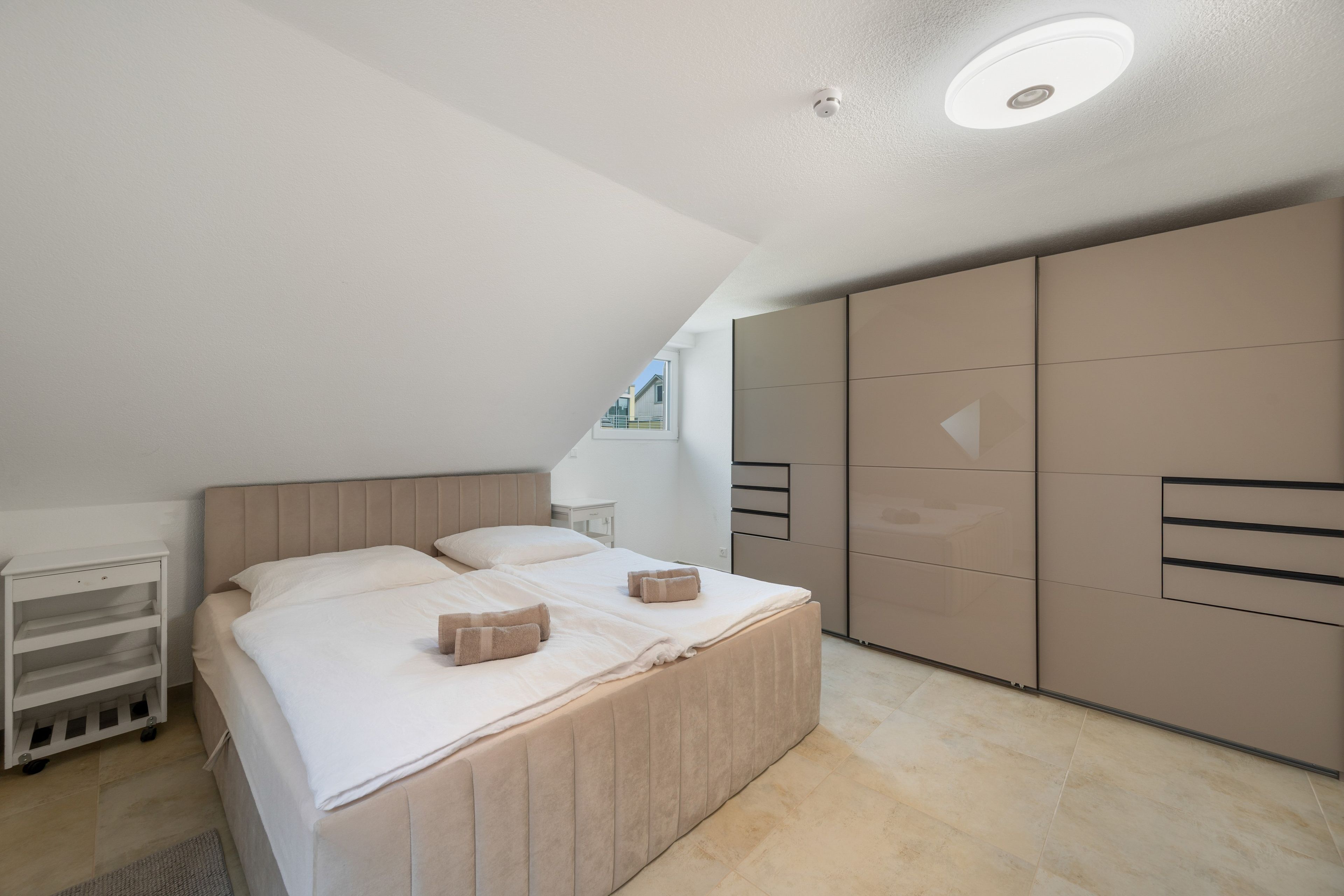 A bedroom with a bed, a bedside table, a wardrobe, and a ceiling light.