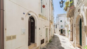 Eine enge Kopfsteinpflasterstraße, gesäumt von weißen Gebäuden mit rundbogigen Portalen und Fenstern, einige mit Fensterläden.