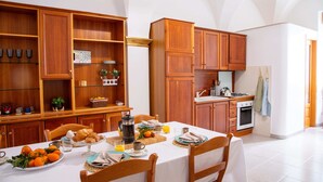 Ein Essbereich mit einem für das Frühstück gedeckten Tisch, Holzausstattung, einer Küchenzeile mit Herd und einem Fliesenboden.