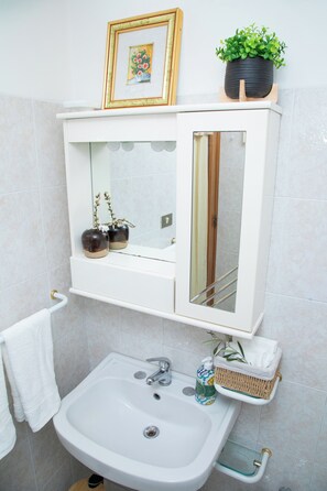 A bathroom with a white sink, a mirror, a framed picture, a potted plant, and a towel rack. - Charming Townhouse in Martina Franca Old Town with Roof Terrace (Martina Franca)