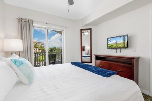 A hotel room with a bed, a TV, a dresser, and a balcony with a view of palm trees and buildings. - Sunset Vistas Getaway (Treasure Island)