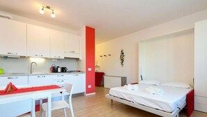 A modern room with a bed, a desk, and a kitchenette. - Studio Laura - Corte Fasanella (Toscolano Maderno)
