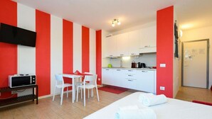 A room with a bed, a desk, a chair, a microwave, a TV, and a kitchenette. - Studio Laura - Corte Fasanella (Toscolano Maderno)