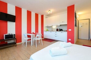 A room with a bed, a desk, a chair, a microwave, a TV, and a kitchenette. - Studio Laura - Corte Fasanella (Toscolano Maderno)