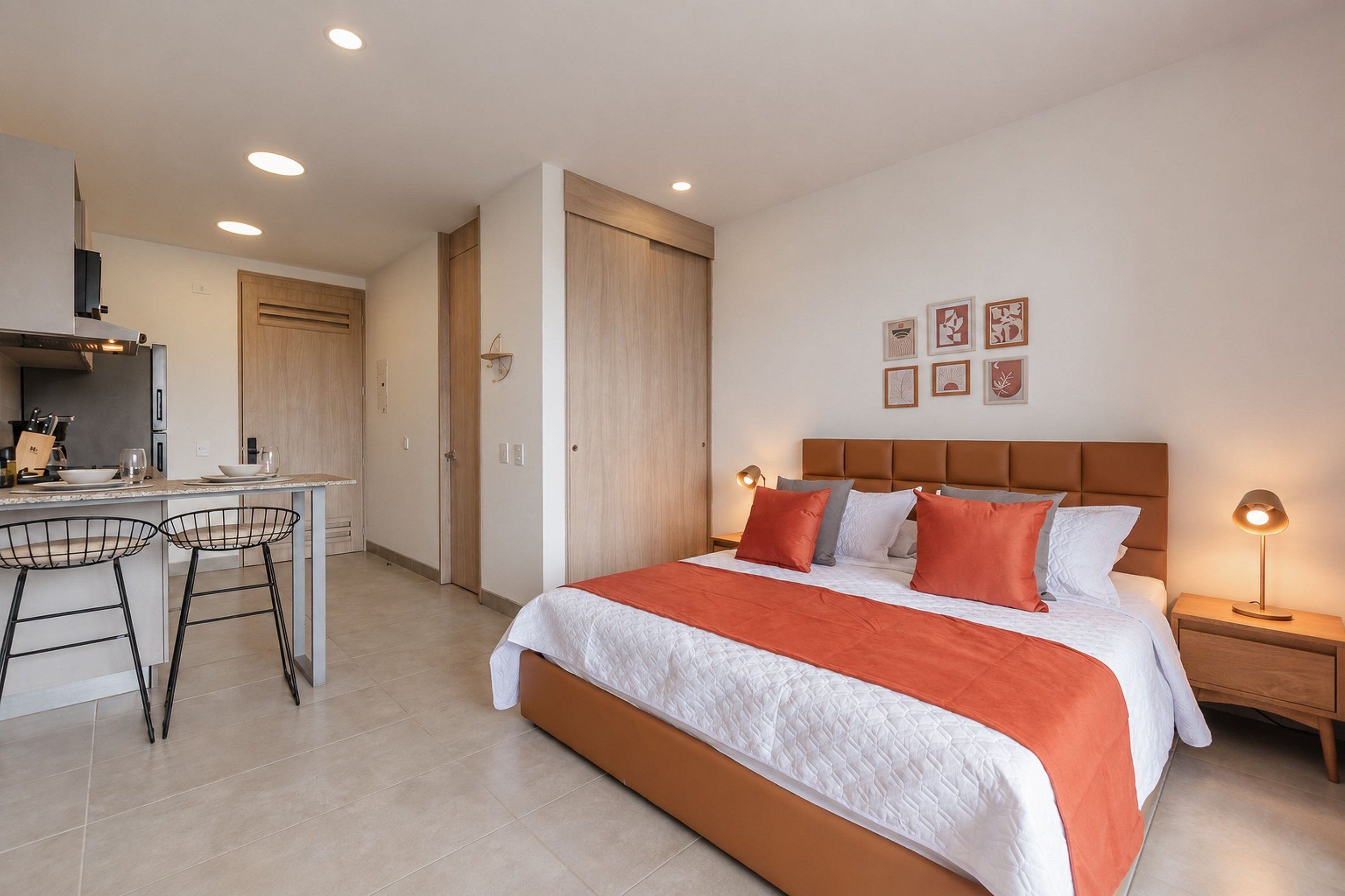 Een moderne slaapkamer met een groot bed, nachtkastjes en een bureau met stoelen.