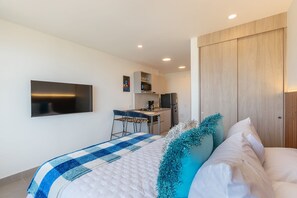 A modern hotel room with a bed, a TV, a kitchenette, and a wooden wardrobe. - U-GO Santa Marina Exclusividad y Mar (Santa Marta)