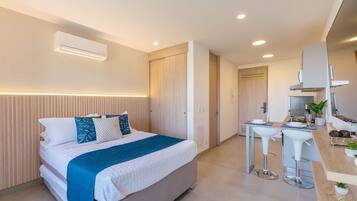 Una habitación de hotel moderna con cama, mesita de noche y una zona de kitchenette.
