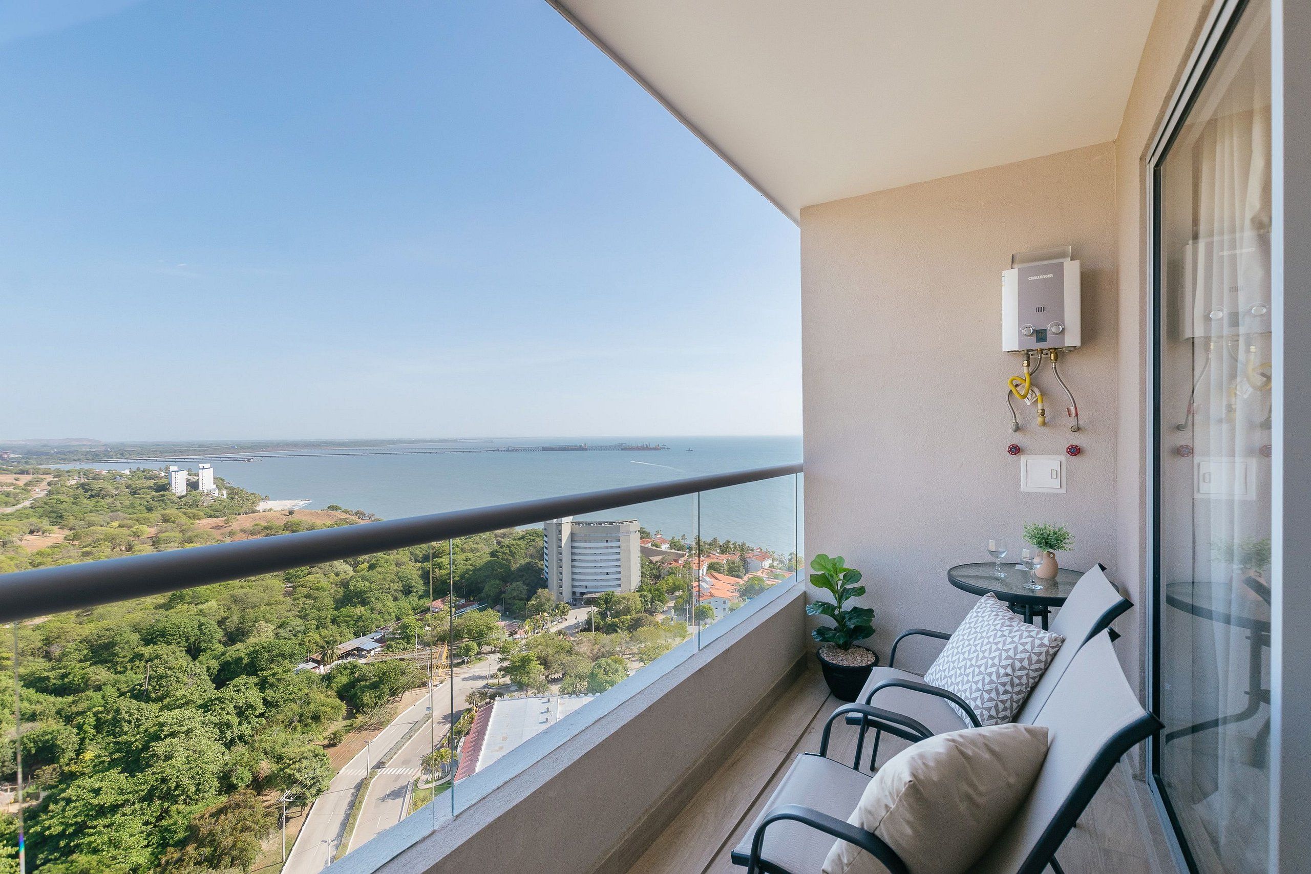 A balcony with a view of a bridge and water, a small table with chairs, and a wall-mounted heater.