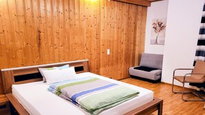 A wooden-paneled room with a bed, a grey sofa, and a metal-framed chair.