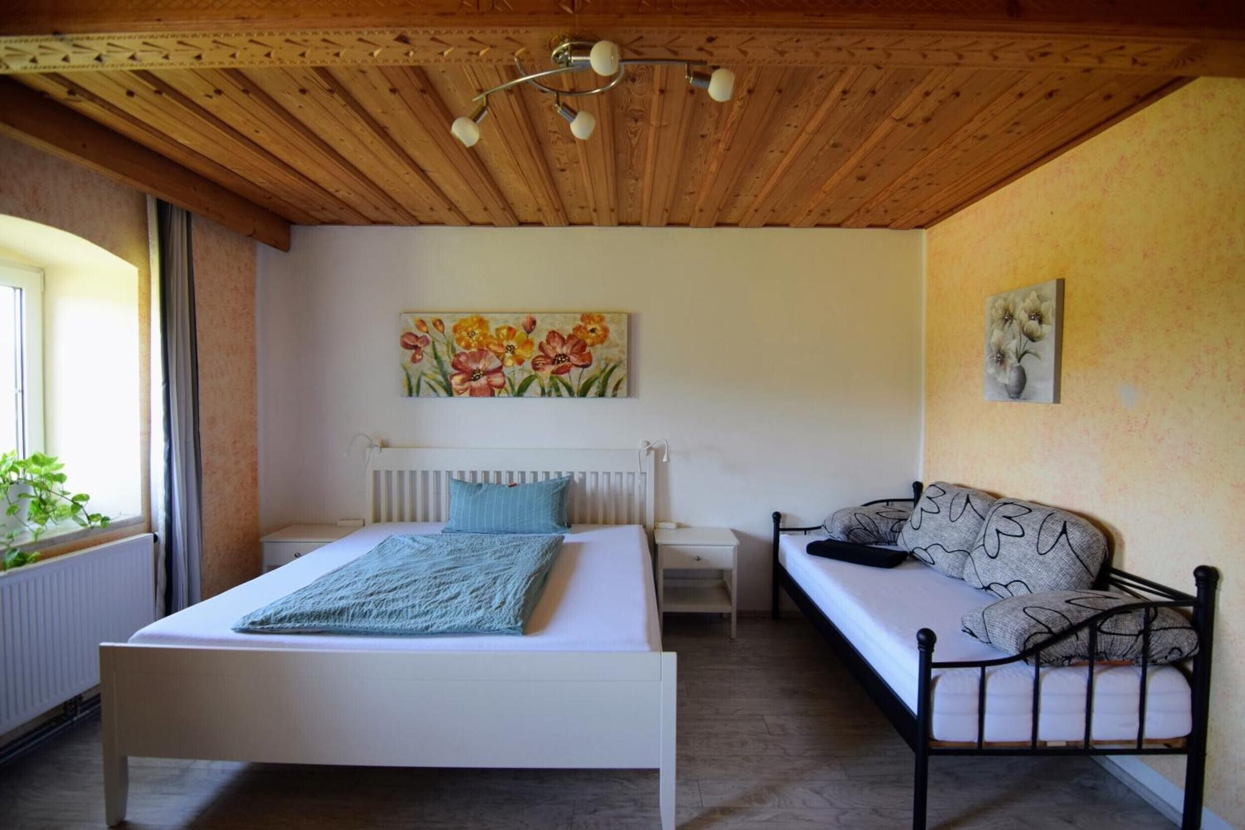 Een slaapkamer met een bed, een slaapbank, een nachtkastje, een schilderij en een plafondventilator.