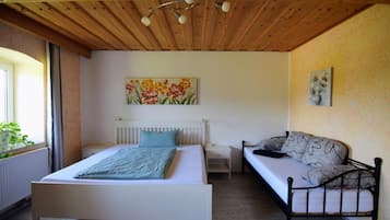 Een slaapkamer met een bed, een slaapbank, een nachtkastje, een schilderij en een plafondventilator.