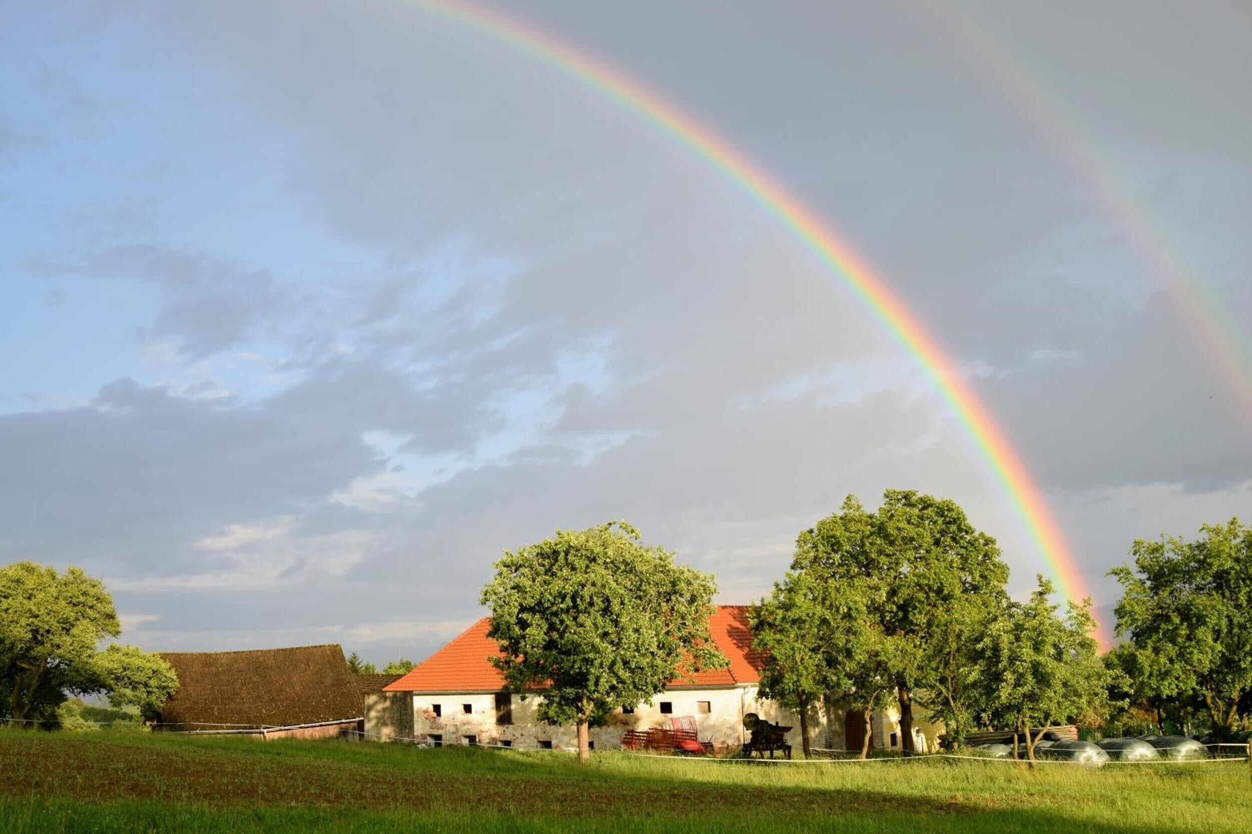 A rural landscape with a house, trees, and a rainbow.