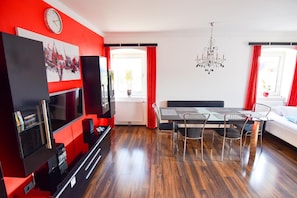 A modern living room with a TV, dining table, chairs, and a chandelier.