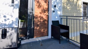 A modern building with a wooden door, a small outdoor seating area, and a metal railing.