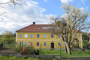 A yellow building with a red roof, surrounded by a fenced garden with trees and a playground.