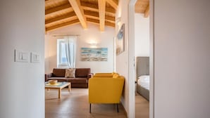 Una habitación con techo de madera, un sofá marrón, un sillón amarillo, una cama y un cuadro en la pared.