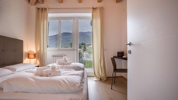 Un dormitorio con cama, escritorio, silla, lámpara y ventana con cortinas.