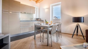 Una cocina moderna con vigas de madera, una mesa de comedor con sillas, un ventanal pequeño y una lámpara trípode.