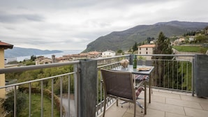 Un balcón con una mesa y una silla, con vistas a un paisaje montañoso y edificios a lo lejos.