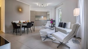 Een moderne woonkamer met een bank, stoelen, een eettafel en een keuken op de achtergrond.