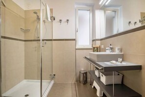 Une salle de bain moderne dotée d’une douche à parois de verre, d’un meuble-lavabo avec un miroir et d’une fenêtre laissant entrer la lumière naturelle.